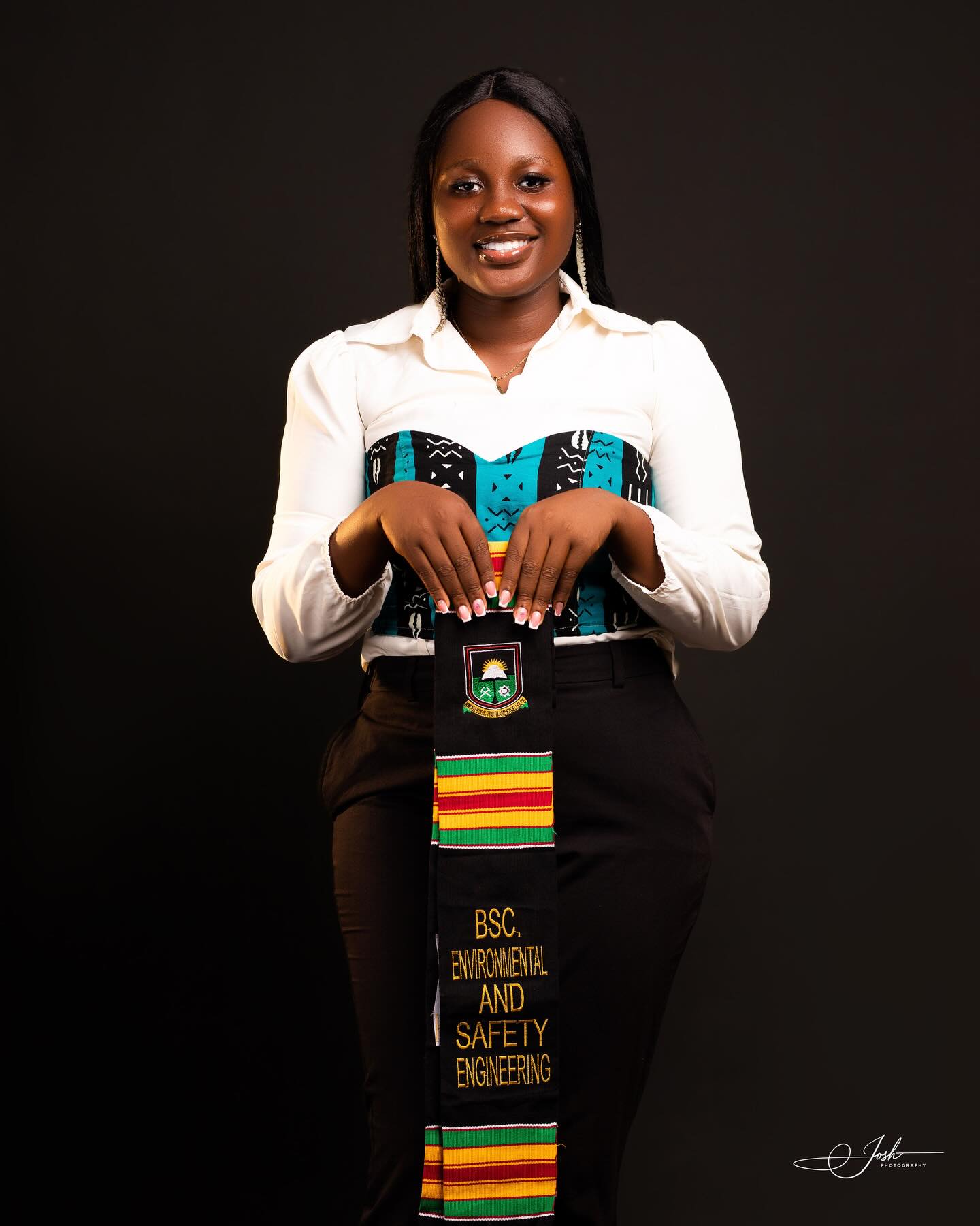 Female graduate in studio holding her kente graduation stole, composed and elegant against black background