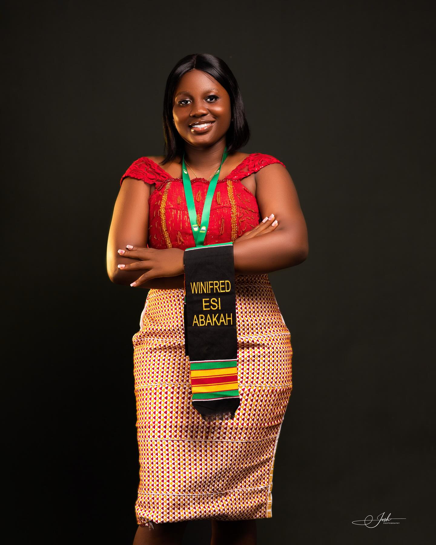 Graduate Winifred Esi Abakah in traditional kente and red lace dress, arms folded confidently in studio — Josh Photography
