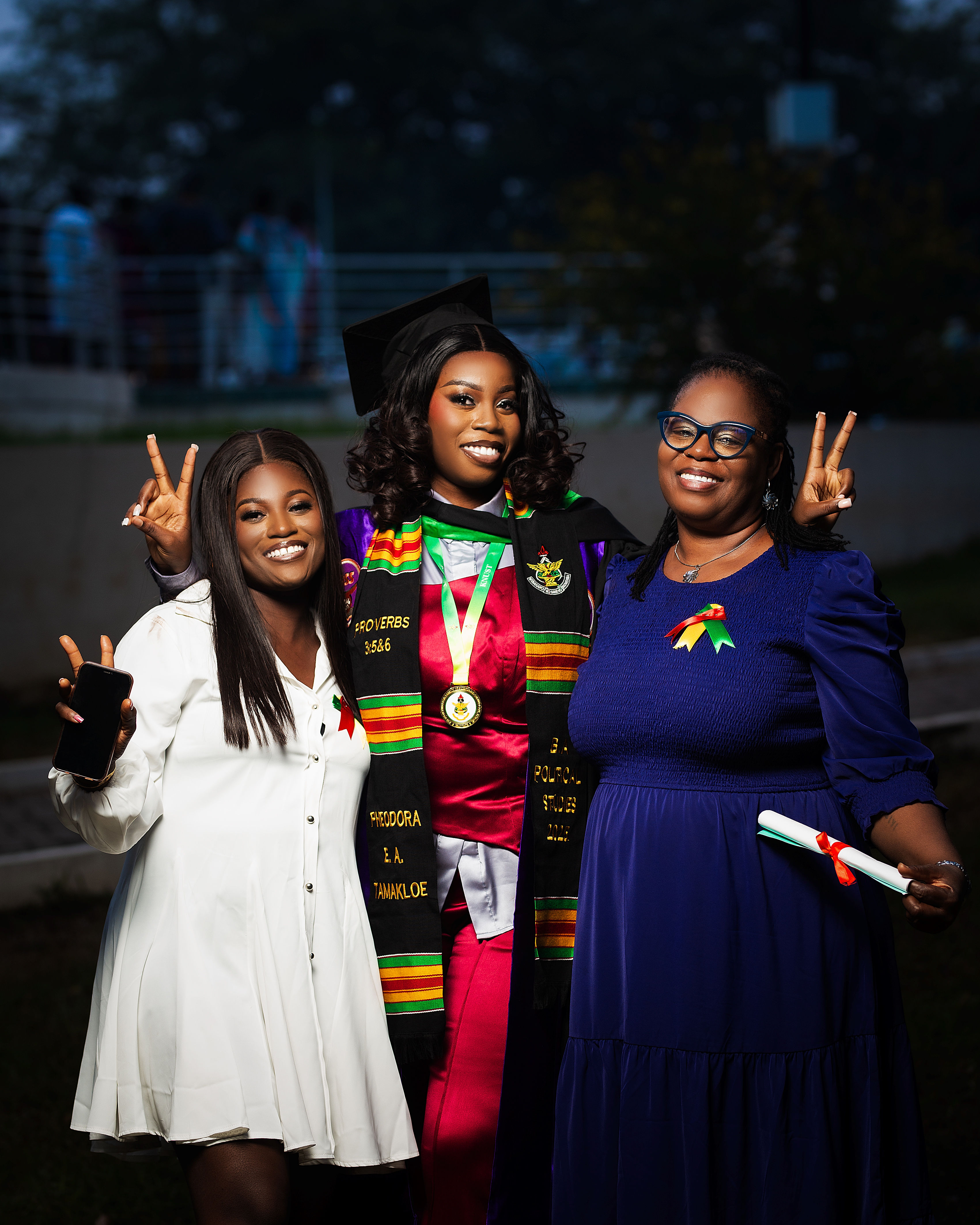 Graduate Pheodora Tamakloe flanked by her sister and mother, all throwing peace signs at night