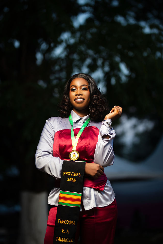 Graduate Pheodora Tamakloe in kente stole and medal, fist raised in a confident solo pose