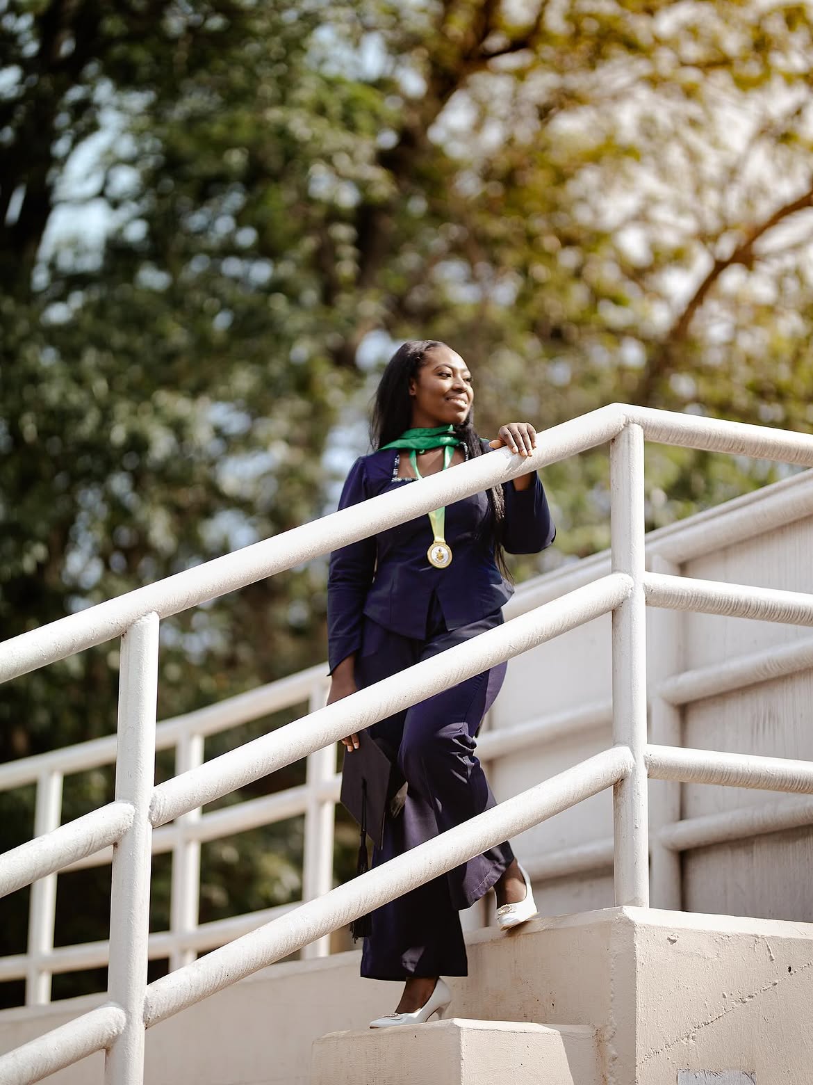 Black-and-white photograph of a female graduate raising her mortarboard cap on campus stairs