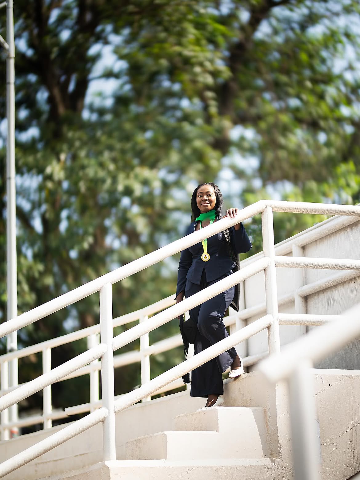 Female graduate on campus stairs, looking directly at the camera — a moment that stays