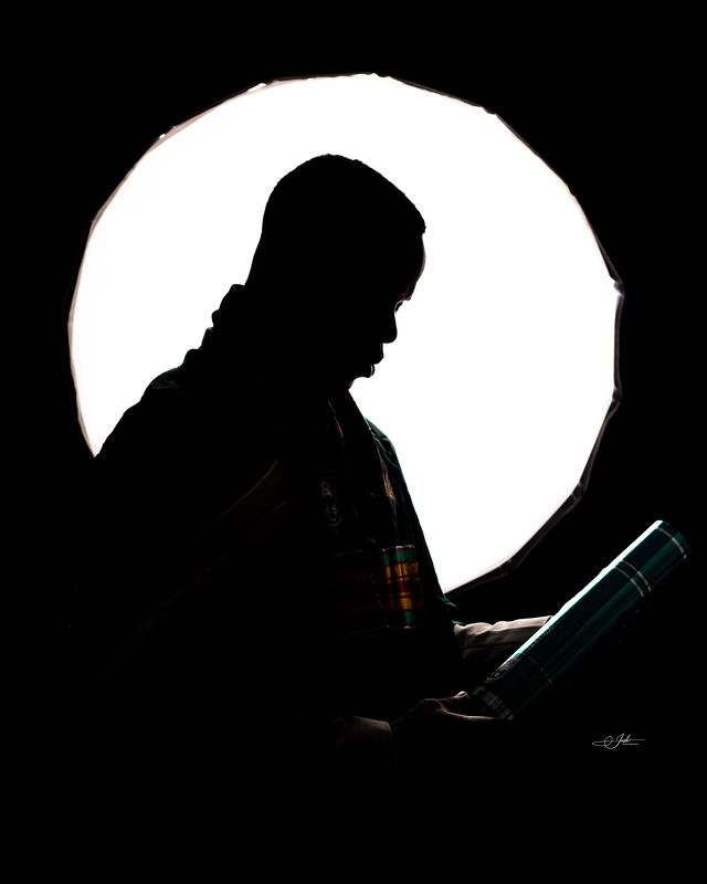 Graduate silhouetted against a circular backlight, holding a degree scroll — cinematic and dramatic