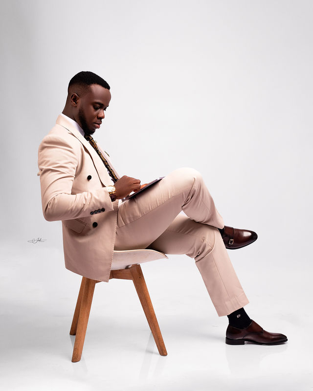 Man in cream double-breasted suit seated in a studio chair, reading — composed and editorial